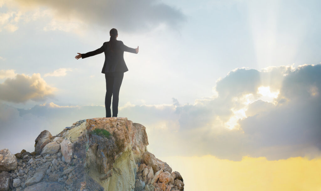 Young woman standing on the top of rock and open hands towards the sun. Success in business concept