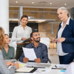 Group of mixed race business people discussing work in conference room. Senior business manager guiding employees in meeting. Group of businessman and businesswoman working together while brainstorming and sharing new ideas and strategy.