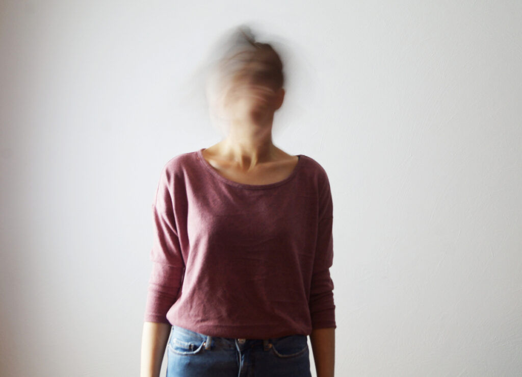 Portrait of confused young woman with blurred face. She is moving her head fast, so her face isn't identifiable. Motion blur.