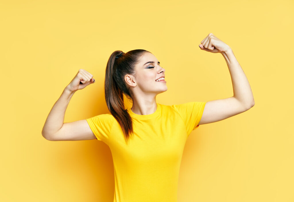Powerful confident young woman showing arms muscles on yellow background. Woman power. Confident and proud female, success pose, Fitness concept.