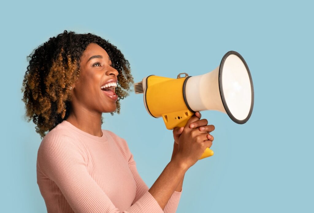 Announcement Concept. Cheerful Black Woman Shouting With Megaphone In Hands, Curly African American Lady Holding Loudspeaker, Sharing News, Standing Isolated On Blue Background, Panorama, Copy space