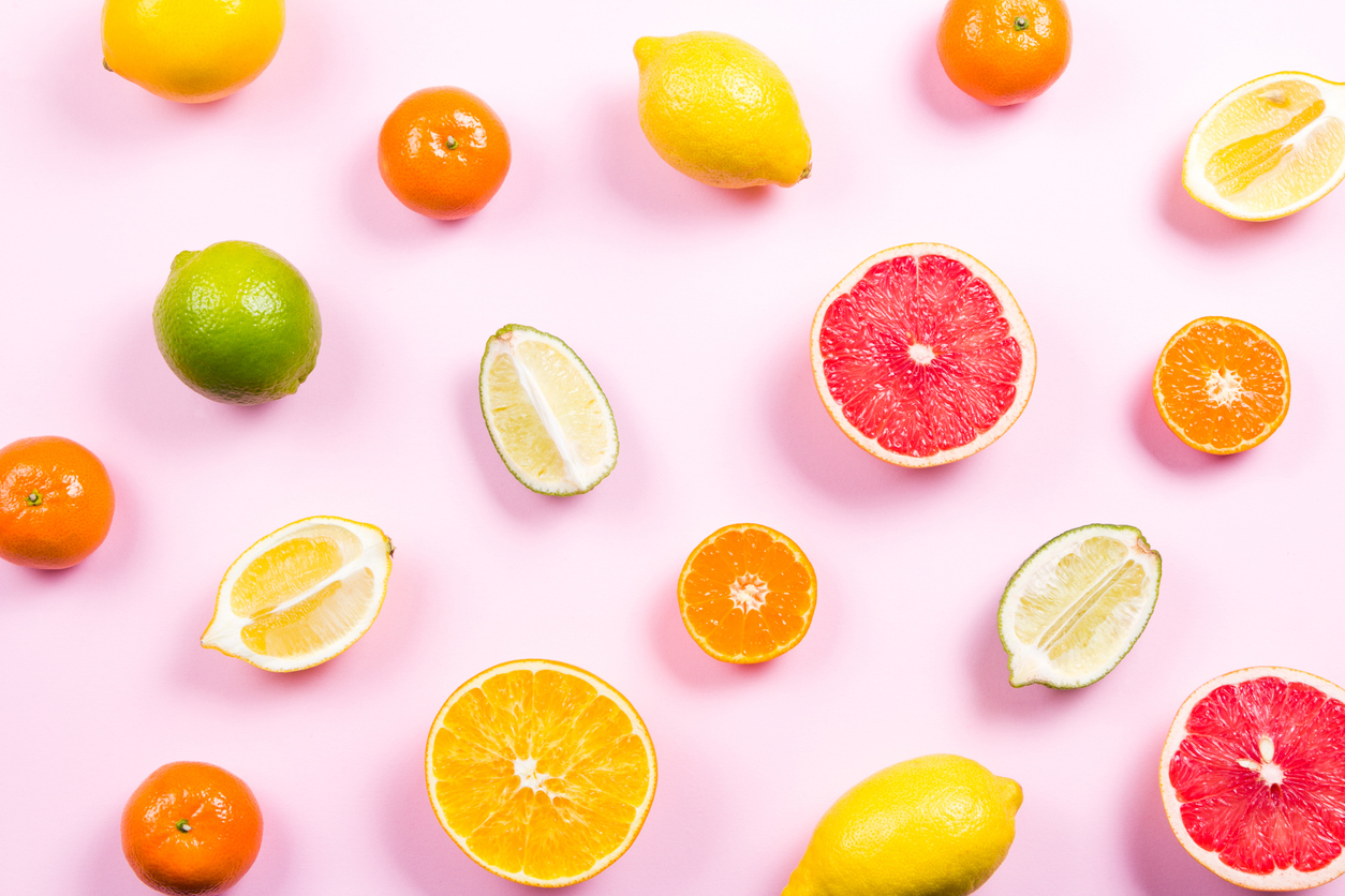 Several kinds of whole and cut citrus on a pink background. Top view