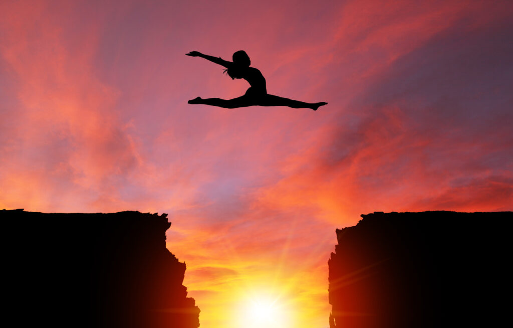Silhouette of girl dancer in a split leap over dangerous cliffs with dramatic sunset or sunrise background and copy space. Concept of faith, conquering adversity, taking risk; challenge, courage, determination or achievement.  Please note the sunset background was shot in Calgary on 10-24-2017 (reference image attached).  The dancer model was shot in studio on 04-07-2016 (Reference image attached and Model Release also attached). The dance model was isolated in Photoshop and then composited onto the sunset background as a silhouette.